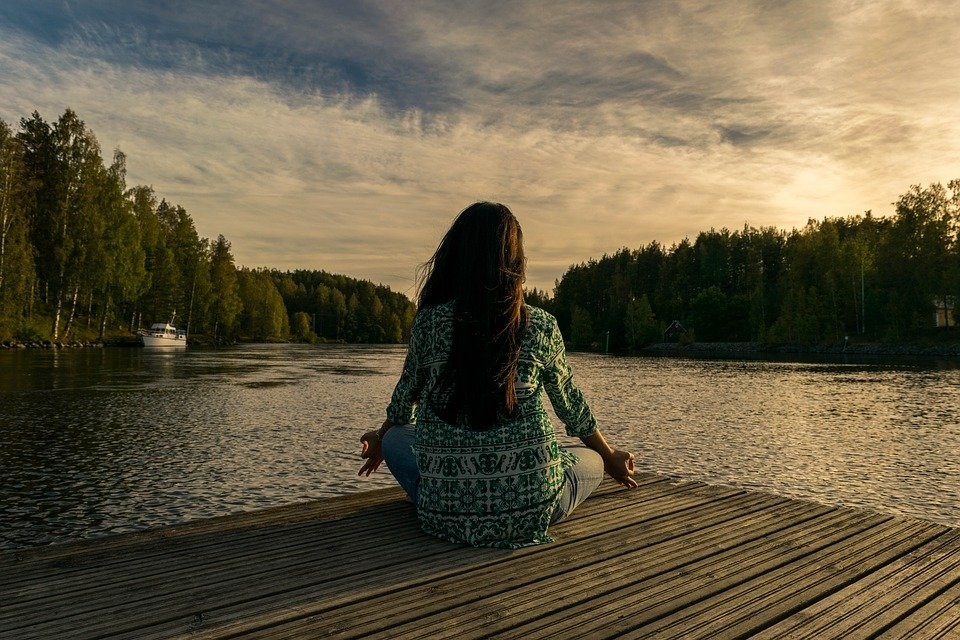 A student meditating. Meditation is a fantastic way to stay in the moment, keep perspective and practice mindfulness. The student is sat on a pier overlooking a lake - the scene is clearly relaxing. 