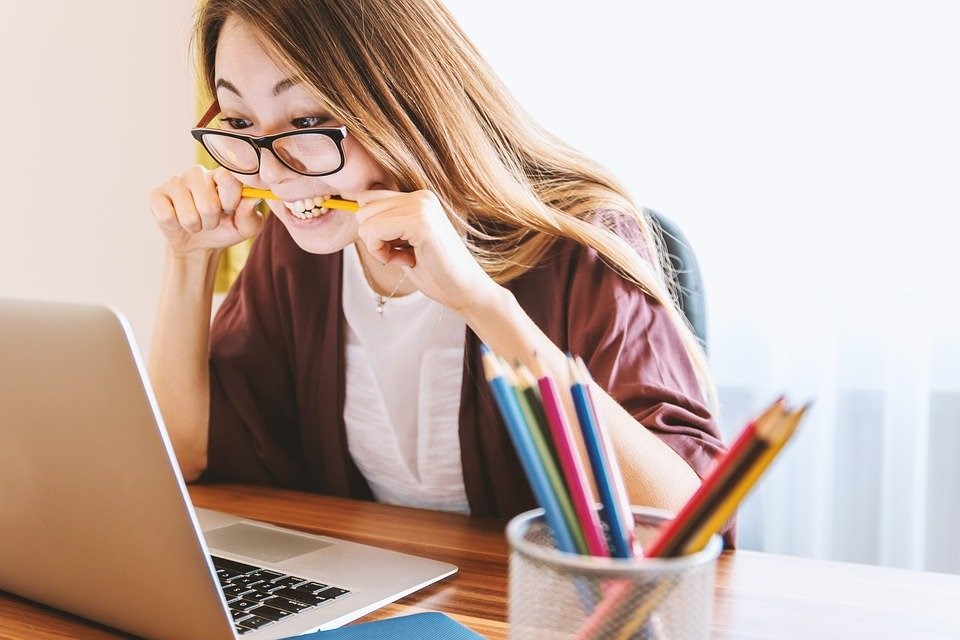 A student is biting their pencil while working on a computer. They are clearly stressed with their studies. 