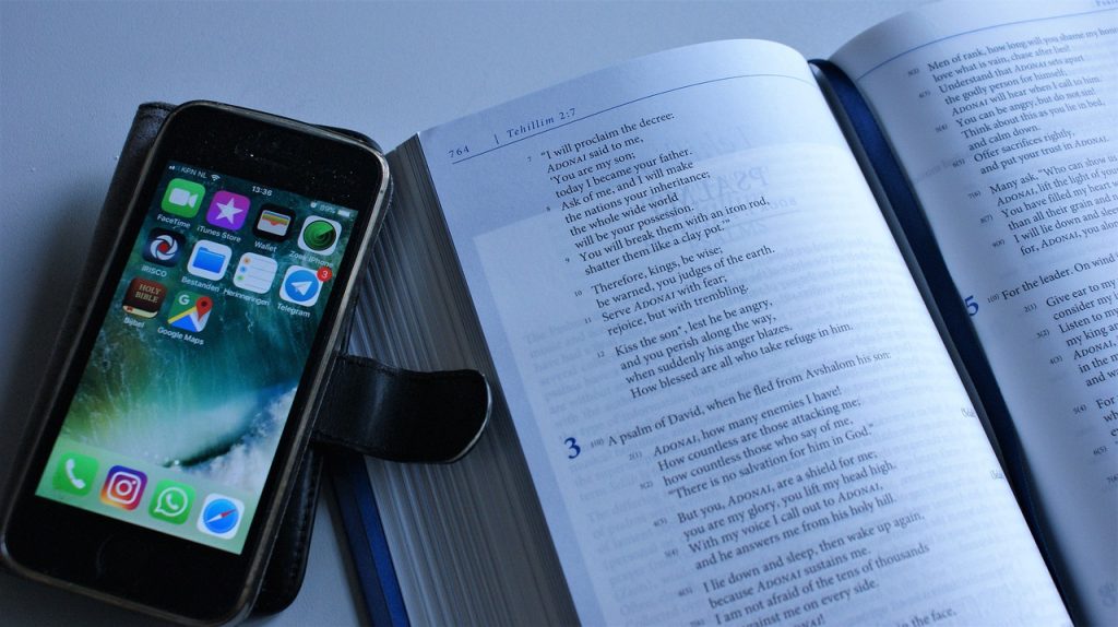 A photograph of a mobile phone sitting on top of a book. This kind of set up leads to procrastination! Put the phone away and out of sight. 